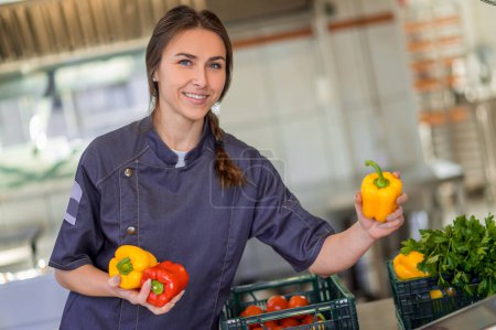 Photo for In the kitchen. Young smiling woman with peppers in hands in the kitchen - Royalty Free Image