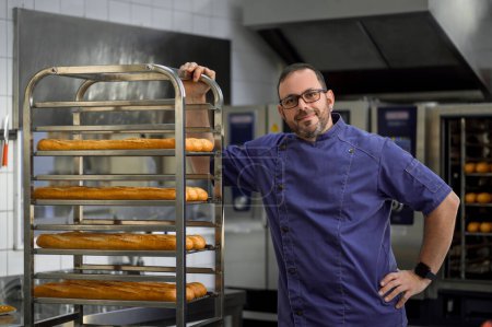 Téléchargez les photos : Homme boulanger debout près des étagères avec des baguettes dans la boulangerie - en image libre de droit