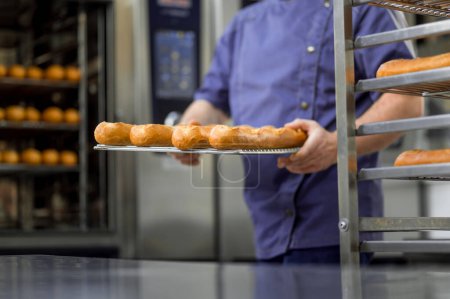 Téléchargez les photos : Boulanger professionnel méconnaissable à la boulangerie avec baguette de pain au boulanger - en image libre de droit