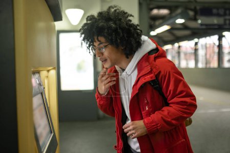Téléchargez les photos : À la gare. Homme aux cheveux bouclés se tenant près du distributeur et le regardant - en image libre de droit