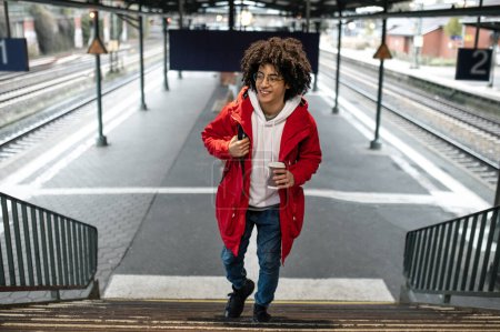 Téléchargez les photos : Voyageur. Jeune homme aux cheveux bouclés en veste rouge à la gare - en image libre de droit