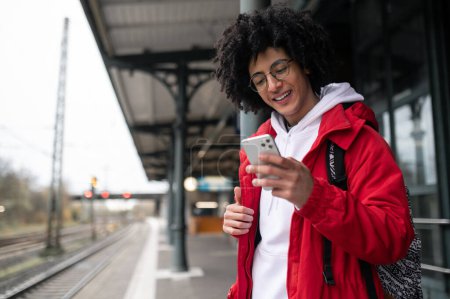 Photo for At the railway station. Curly-haired guy in eyeglasses with a phone in hands at the railway platform - Royalty Free Image