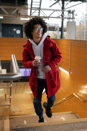 Téléchargez les photos : À la gare. Voyageur en veste rouge prenant un café et attendant le train - en image libre de droit