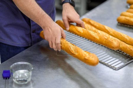 Photo for Unrecognizable man baker baking baguettes in professional bakehouse - Royalty Free Image