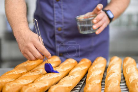 Photo for Unrecognizable man baker in uniform baking baguettes at manufacturing - Royalty Free Image