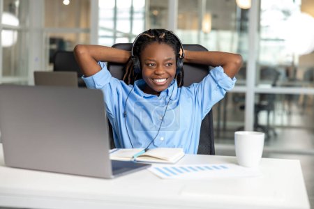 Foto de Atractiva mujer de piel oscura en auriculares que trabajan en el ordenador portátil en el espacio de coworking - Imagen libre de derechos