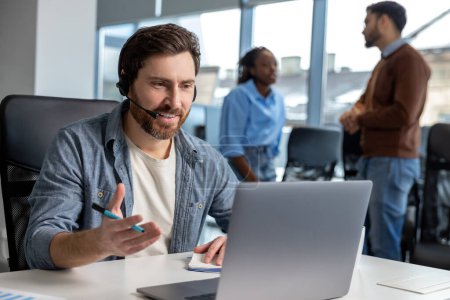 Téléchargez les photos : Homme attrayant dans le casque de travail sur ordinateur portable dans l'espace de coworking - en image libre de droit