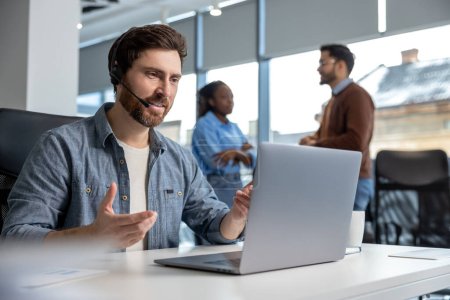 Téléchargez les photos : Homme souriant travaillant dans le centre d'appels au bureau au téléphone avec casque - en image libre de droit