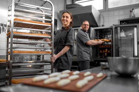 Téléchargez les photos : À la boulangerie. Homme et femme travaillant dans une boulangerie et regardant satisfait - en image libre de droit