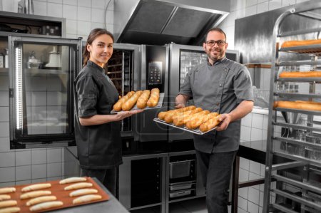 Téléchargez les photos : À la boulangerie. Homme et femme travaillant dans une boulangerie et regardant satisfait - en image libre de droit