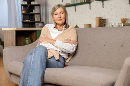 At home. Blonde mid aged woman sitting on the sofa at home