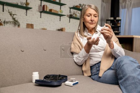 Photo for Diabetic woman. Mature blonde woman making home blood sugar test - Royalty Free Image