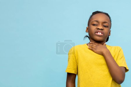 Téléchargez les photos : Petit garçon malsain à la peau foncée tenant un cou douloureux isolé sur fond bleu, espace de copie - en image libre de droit