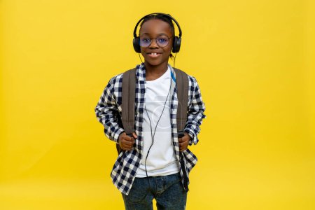 Téléchargez les photos : Un écolier. Mignon écolier afro-américain en tshirt à carreaux regardant heureux - en image libre de droit