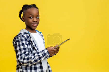 Téléchargez les photos : Un écolier. Garçon à la peau foncée d'âge scolaire avec une tablette dans les mains - en image libre de droit
