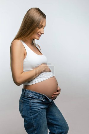 Téléchargez les photos : Une femme enceinte. Femme enceinte souriante en jeans et tshirt blanc - en image libre de droit