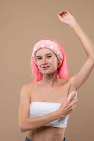 Téléchargez les photos : Rose cheveux jeune femme pulvérisation déodorant sur son corps après la douche - en image libre de droit