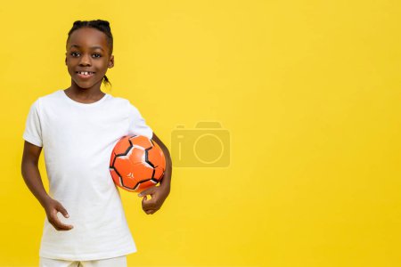 Photo for Little cheerful African American boy playing football on kids championship isolated over yellow background, copy space - Royalty Free Image