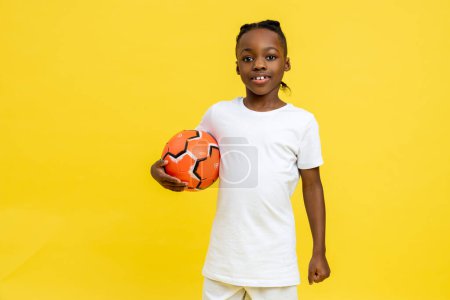 Téléchargez les photos : Mixte-race petit garçon ayant entraînement de football avec ballon isolé sur fond jaune - en image libre de droit