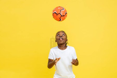Foto de Joven chico multicultural en ropa deportiva jugando con pelota de fútbol aislado sobre fondo amarillo, espacio de copia - Imagen libre de derechos
