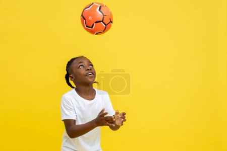 Foto de Niño de raza mixta que tiene entrenamiento de fútbol con pelota aislada sobre fondo amarillo, espacio de copia - Imagen libre de derechos