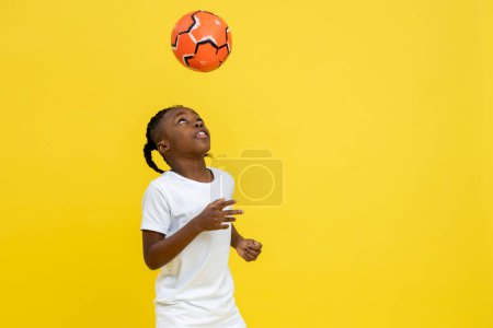 Photo for Playful little mixed-race boy doing tricks with soccer ball isolated over yellow background, copy space - Royalty Free Image
