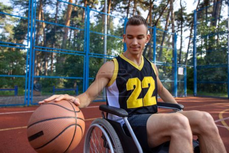 Jeune athlète homme ayant un handicap en fauteuil roulant ayant l'entraînement de basket sur le terrain de jeu d'été