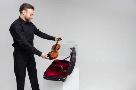 Téléchargez les photos : Homme barbu artiste emballage instrument de musique dans une caisse de violon isolé sur fond blanc - en image libre de droit