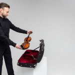 Bearded man artist packing musical instrument in violin case isolated on white background
