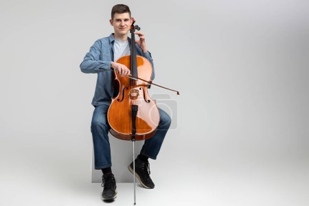 Photo for Attractive man musician playing cello on concert isolated over light gray background - Royalty Free Image