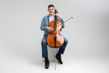 Photo for Young man wearing casual clothing playing cello isolated over white background - Royalty Free Image