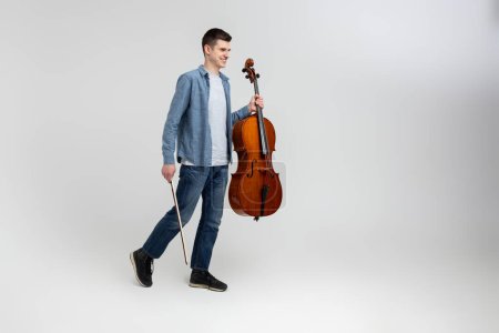 Photo for Handsome man musician playing cello on concert isolated over light gray background - Royalty Free Image