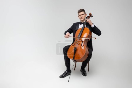 Photo for Passionate cello player sitting on chair performing concert isolated over white background - Royalty Free Image
