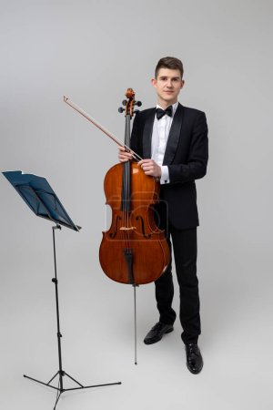 Téléchargez les photos : Pleine longueur de jeune musicien masculin jouant avec violoncelle et note de musique isolé sur fond blanc - en image libre de droit