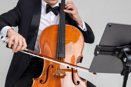 Téléchargez les photos : Musicien masculin méconnaissable jouant avec violoncelle et note de musique isolé sur fond blanc - en image libre de droit