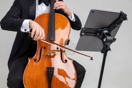 Téléchargez les photos : Homme artiste méconnaissable portant un smoking jouant du violoncelle avec une note de musique isolée sur fond blanc - en image libre de droit