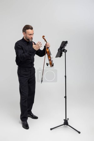 Foto de Longitud completa del músico tocando el violín tocando concierto de pie aislado sobre fondo gris claro - Imagen libre de derechos