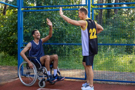 Foto de Silla de ruedas jugador de baloncesto hombre jugando partido de competición con un amigo en la cancha al aire libre - Imagen libre de derechos