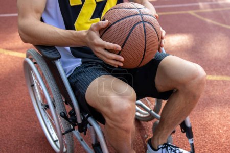 Téléchargez les photos : Homme anonyme joueur de basket en fauteuil roulant tenant ballon de basket sur le court d'été - en image libre de droit