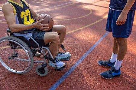Foto de Jugador de baloncesto en silla de ruedas en una cancha al aire libre jugando con un amigo - Imagen libre de derechos