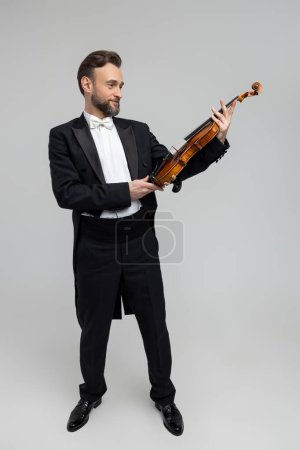 Téléchargez les photos : Elégant homme barbu avec instrument pour violon isolé sur fond gris clair, espace de copie - en image libre de droit