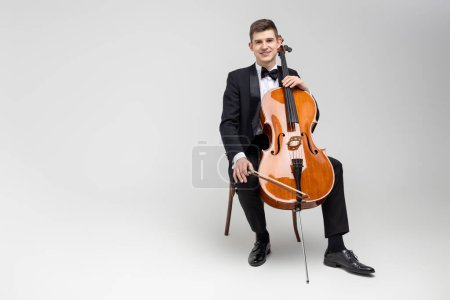 Photo for Young male artist sitting on chair and playing contrabass isolated over white background - Royalty Free Image