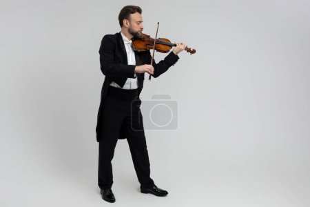 Téléchargez les photos : Homme barbu joueur de violon passionné à la performance de musique classique isolé sur fond gris clair, espace de copie - en image libre de droit