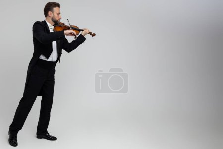 Photo for Elegant man violinist on stage performing concert isolated over light gray background, copy space - Royalty Free Image
