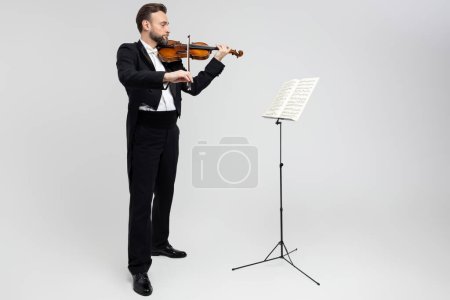 Téléchargez les photos : Violoniste accompli guidé par des partitions de musique classique isolée sur fond blanc - en image libre de droit