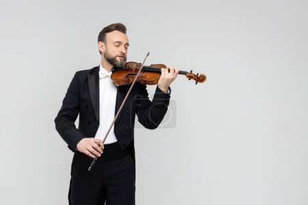 Téléchargez les photos : Homme barbu violoniste artistique se produisant isolé sur fond gris clair, espace de copie - en image libre de droit