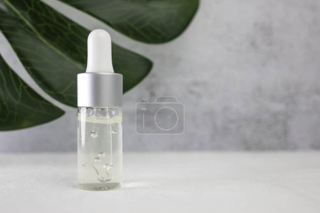 Photo for Dropper bottle with a clear gel-like liquid and a green leaf of a natural plant on a light gray background. Side view, space for text. - Royalty Free Image