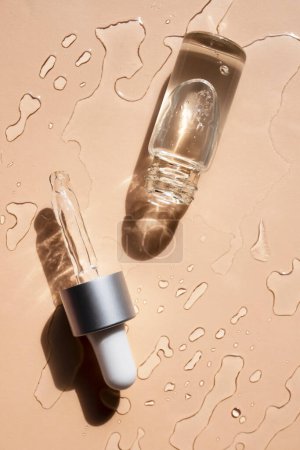 Glass bottle and pipette in a cosmetic transparent liquid on a beige background. Flat lay, vertical image.