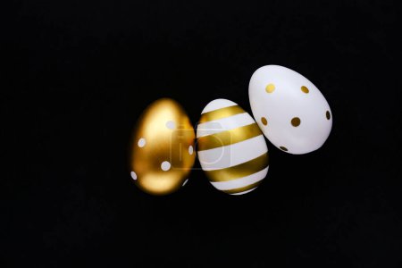 Foto de Huevos de Pascua dorados sobre un fondo negro. Concepto festivo de Pascua. Estilo plano, espacio para texto. - Imagen libre de derechos