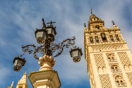 La Giralda (translated to The Giralda), the bell tower of Seville's Cathedral next to the ornate old metallic streetlamps, Spain